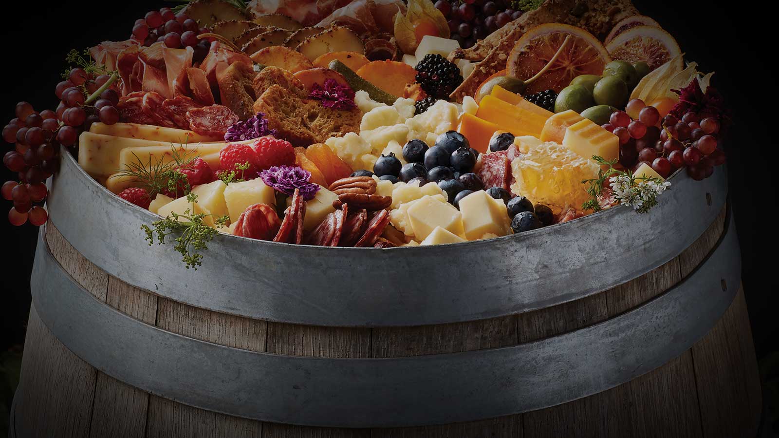 A wooden barrel topped with an assortment of cheeses, meats, fruits and breads.