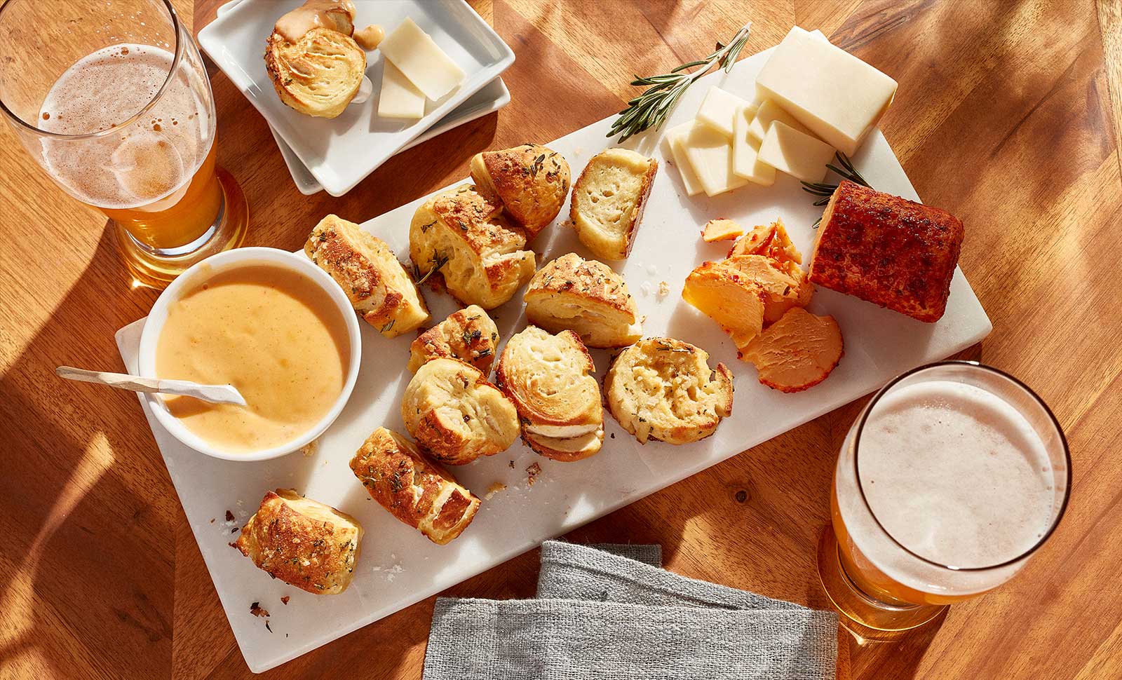A board filled with cheesy herb pretzel bites, cheese logs and dips.