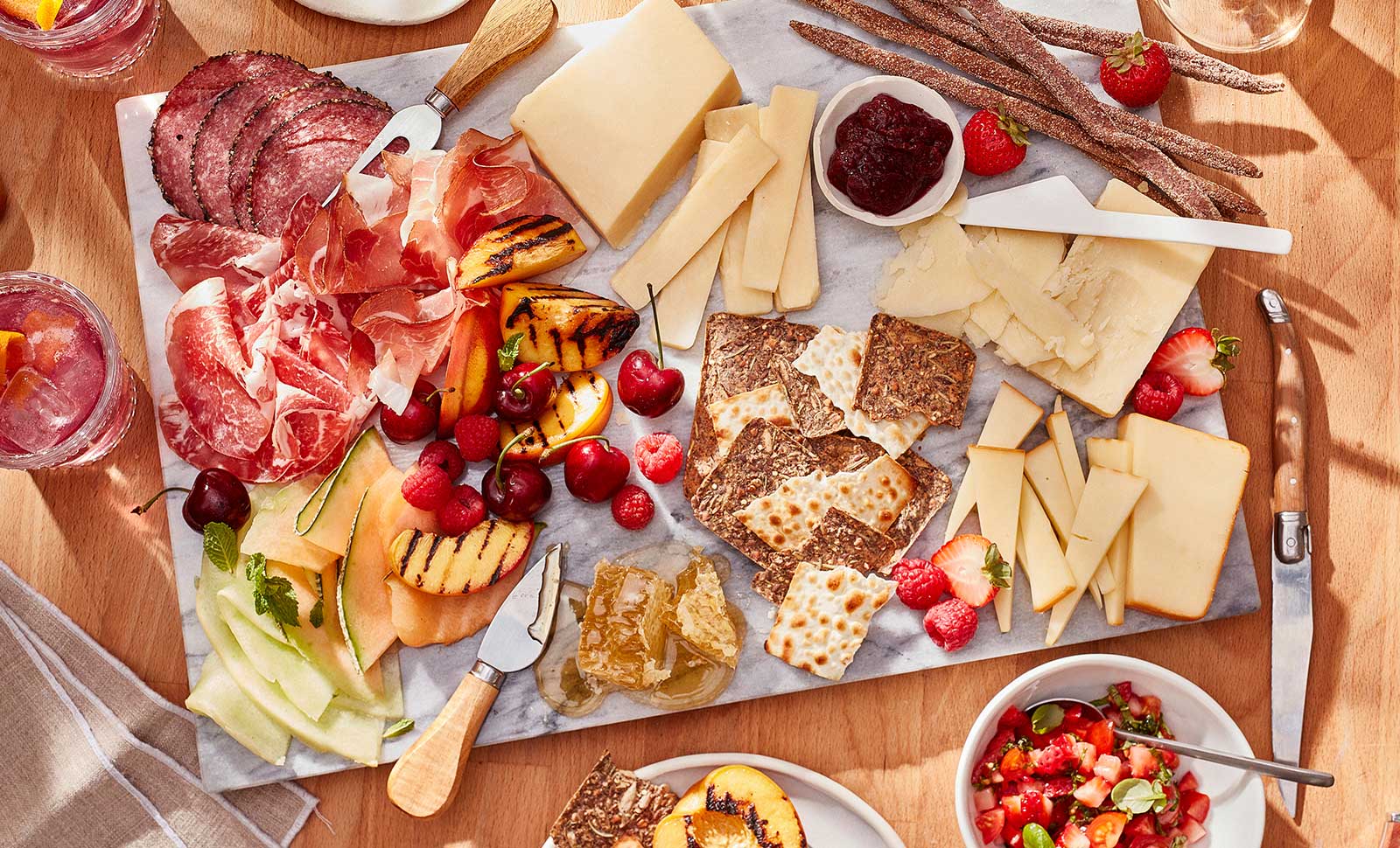 A summer inspired charcuterie board with aged cheddars, slices of salami and prosciutto, crackers, raspberries and cherries.