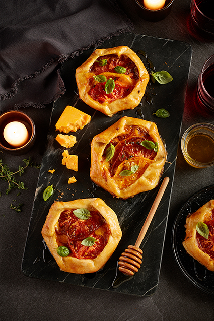 Three mini tomato cheese galettes with lavender honey along with pieces of cheddar cheese.