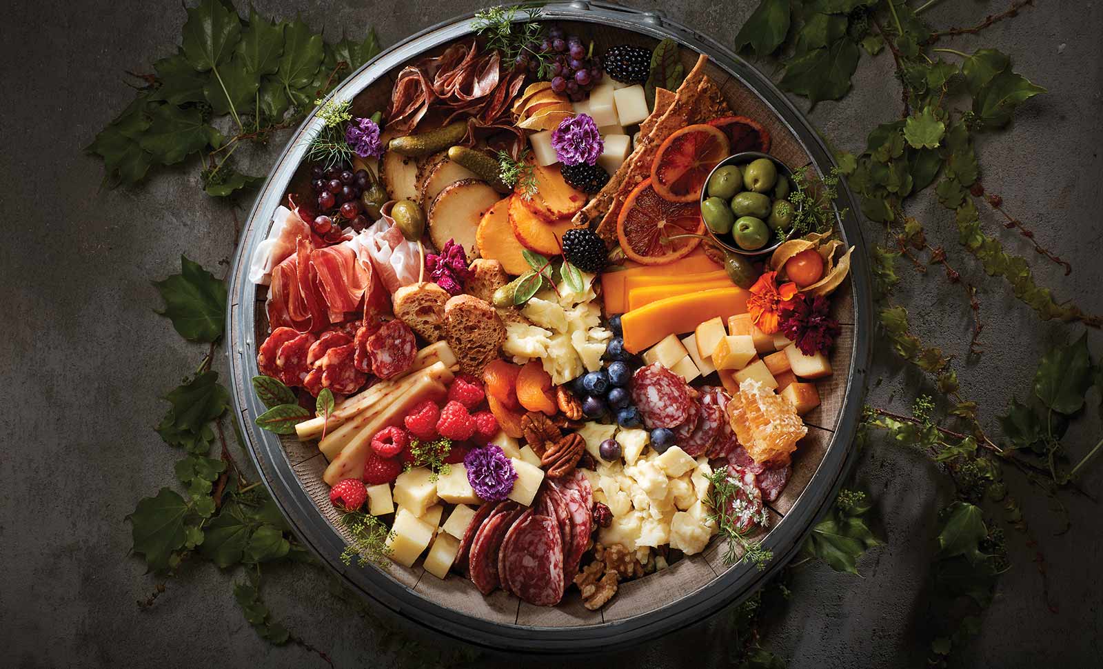 A wooden barrel topped with an assortment of cheeses, meats, fruits and breads