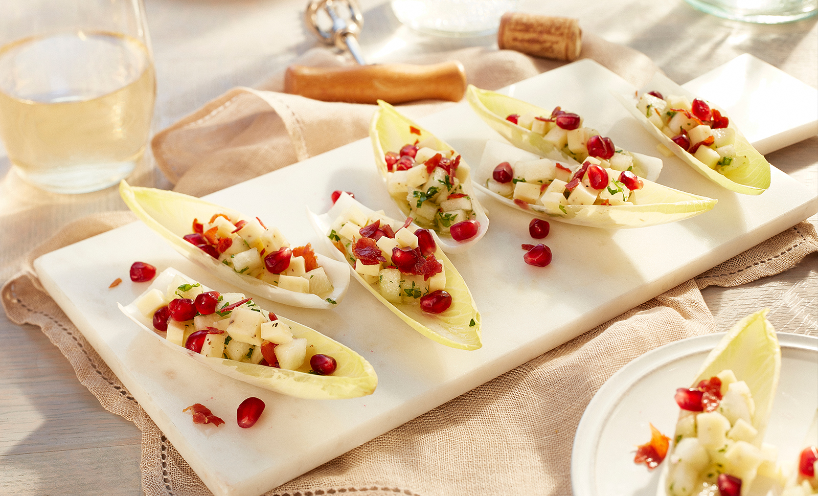 Seven pieces of endive leaves pear salad on a white plate served with a glass of white wine.